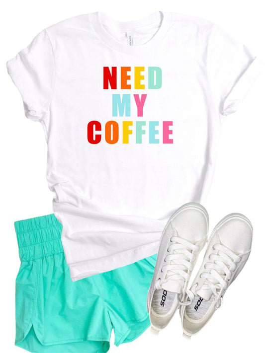 Need My Coffee graphic t-shirt flat lay featuring a white crew neck tee with colorful "NEED MY COFFEE" text, paired with mint green shorts and white sneakers. Soft combed and ring-spun cotton casual coffee lover graphic tee for everyday wear. NEED MY COFFEE Crewneck Tee 100% Combed and Ring-Spun Cotton for Superior Softness