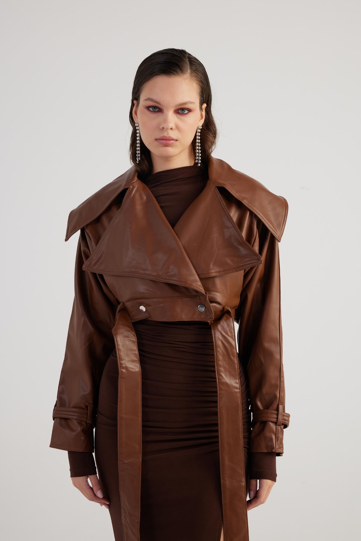 Woman wearing a brown leather jacket over a dress on a white background