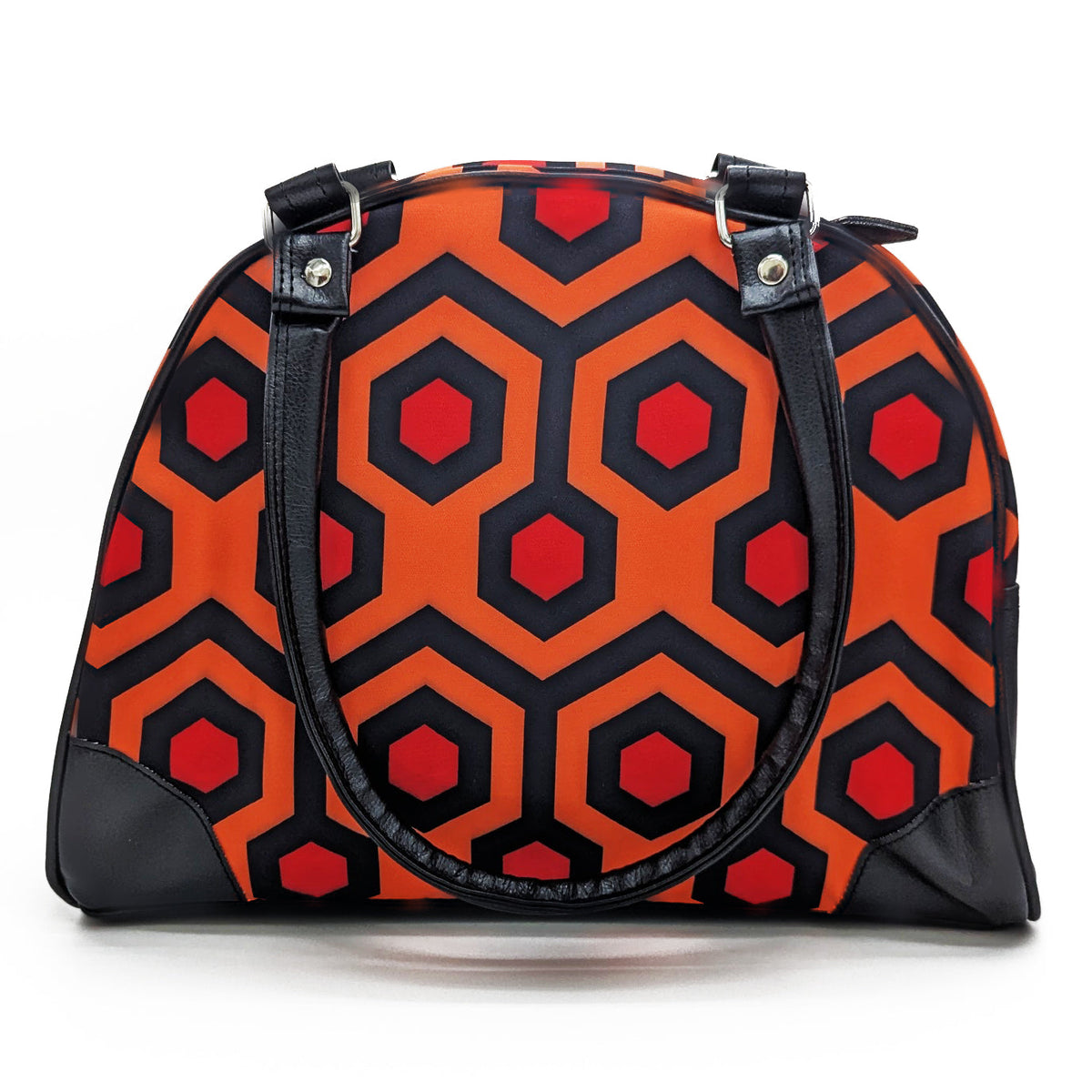 A dome-shaped handbag with a bold geometric pattern of orange, black, and red hexagons, featuring black faux-leather handles and corner protectors on a white background.
