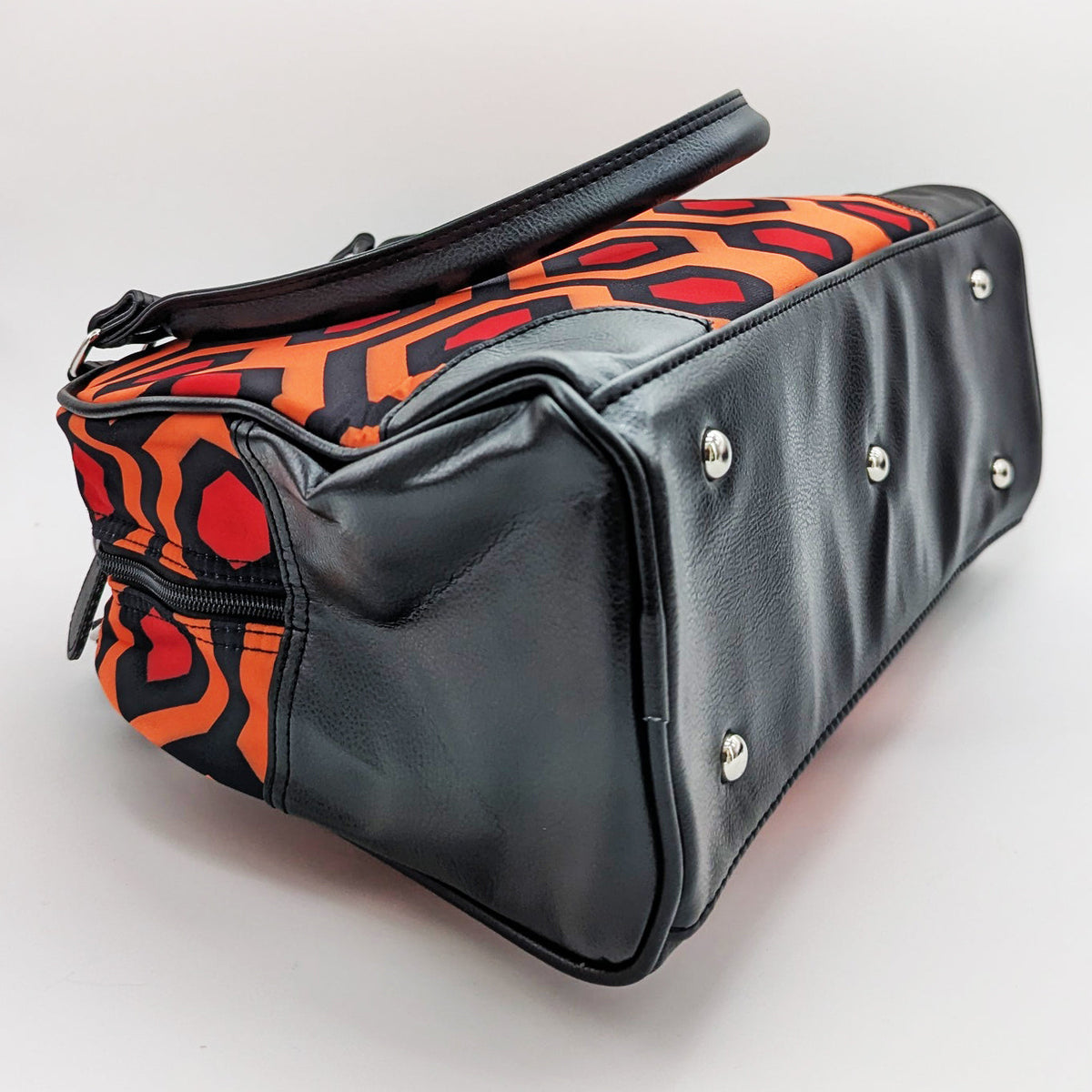 Black handbag with orange and red patterned flap on a light gray background