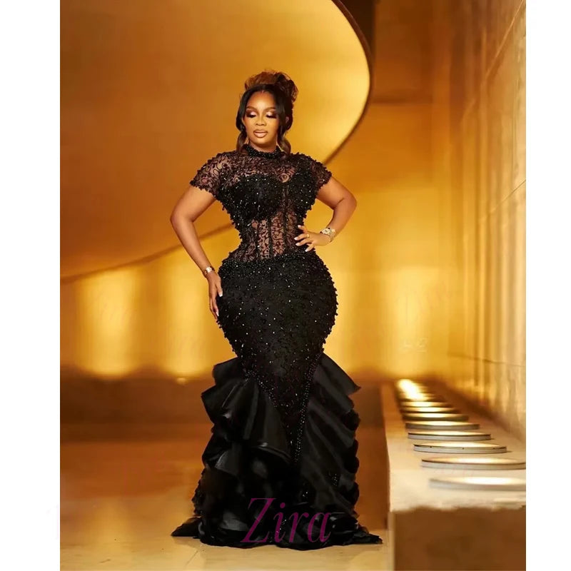 Woman in a black beaded gown standing in a grand hallway with 'Ziva' branding.