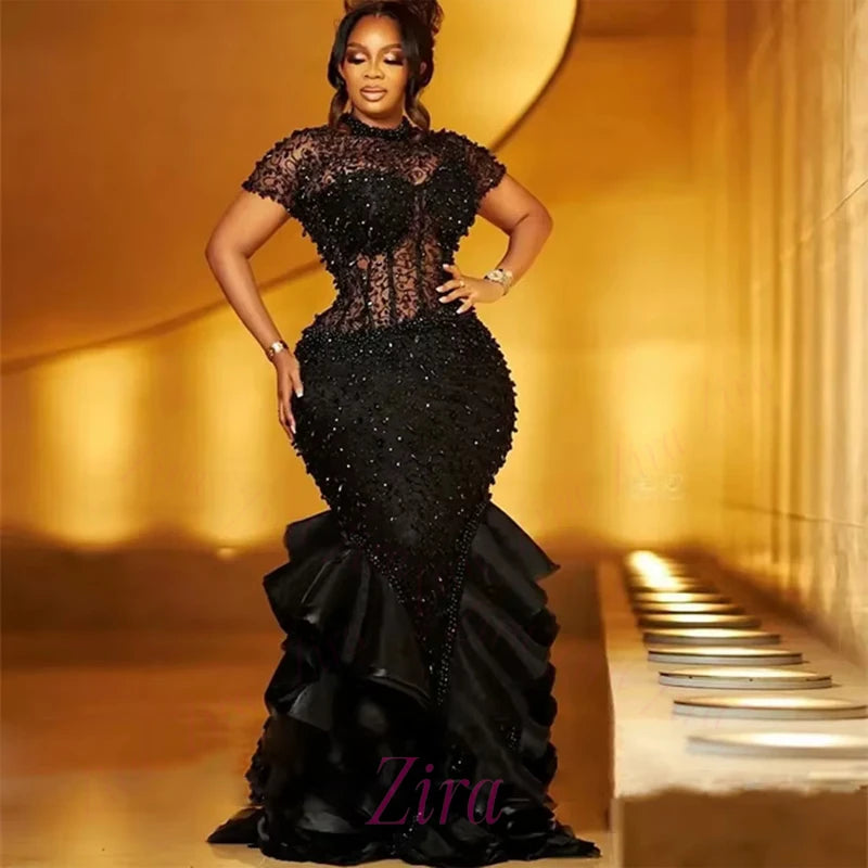 Woman in a black beaded gown standing in a hallway with 'Zira' branding.