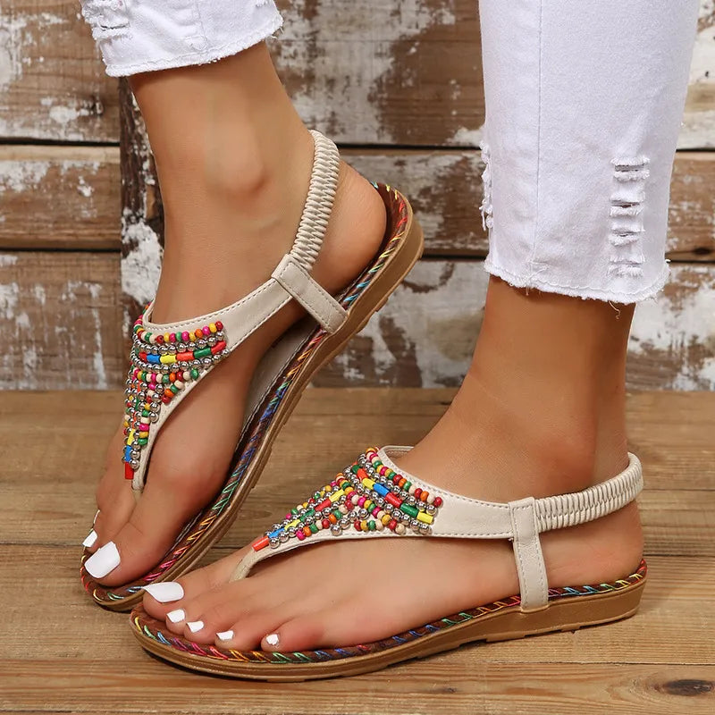 Women's PU leather thong flat sandals with colorful beaded embellishments, elastic slingback strap, braided trim sole, and open-toe design, shown in beige with white distressed jeans.