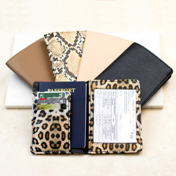 Leopard print passport and vaccine card holder wallet with card slots, clear ID window, and passport sleeve displayed alongside black, beige, taupe, and snakeskin travel wallets on a neutral background.