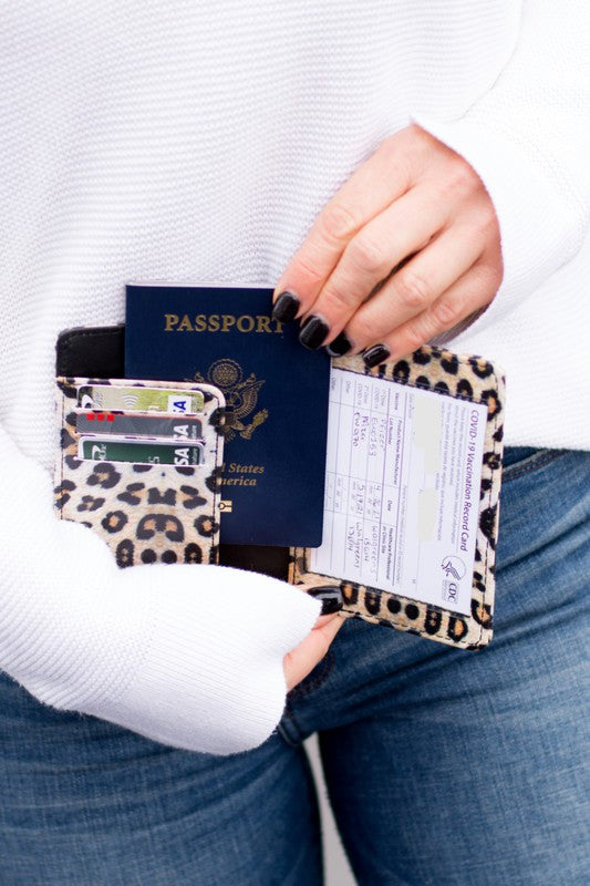 Woman holding an open leopard print passport wallet with a U.S. passport, credit cards, and vaccination card, showcasing multiple travel document and card storage compartments.