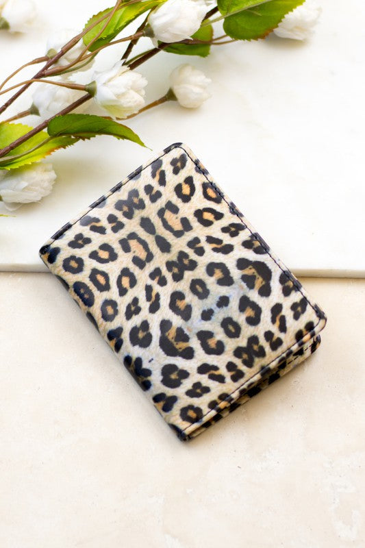 Leopard print passport and vaccine card wallet on a light marble surface with white flowers, compact travel document holder for passports, vaccination cards, credit cards, cash, and travel essentials.
