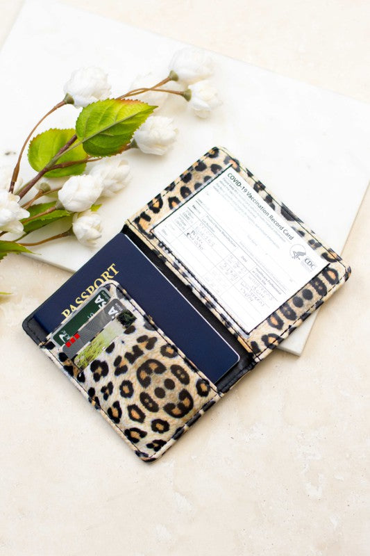 Leopard print RFID passport and vaccine card wallet with passport, credit cards, and vaccination record displayed on a light marble surface beside white flowers, ideal for secure travel document organization.