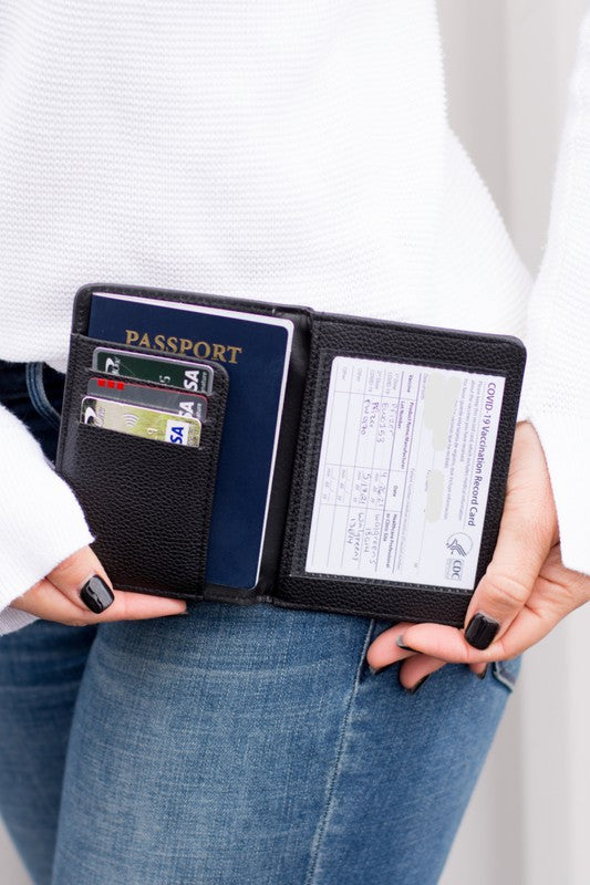 Black RFID passport travel wallet holding a passport, vaccine record card, and multiple credit cards, displayed in hand with slim faux leather design for secure travel organization.
