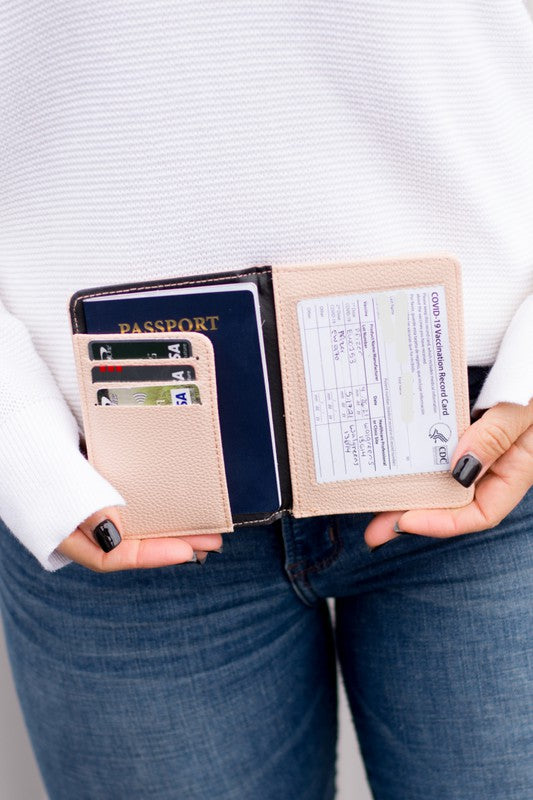 Beige passport and vaccine card wallet holding a passport, credit cards, and CDC vaccination record, displayed in hands against a white sweater and blue jeans, ideal for secure travel document organization.