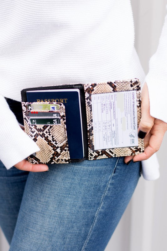 Snake print passport and vaccine card holder wallet with passport, credit cards, and vaccination record displayed, held by person wearing a white sweater and blue jeans. Perfect travel organizer for passports, cards, and travel documents.