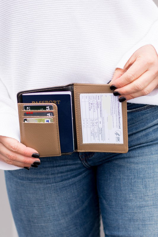 Brown RFID passport travel wallet with passport, credit cards, and vaccine card displayed inside, held open by a person wearing a white sweater and blue jeans, showcasing a slim faux leather travel document organizer for secure travel essentials.