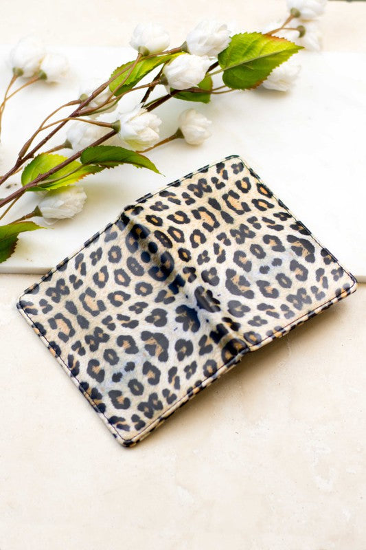 Leopard print passport and vaccine card wallet with a slim bifold design displayed on a light surface with white flowers, ideal for organizing travel documents, passport, credit cards, and vaccination records.