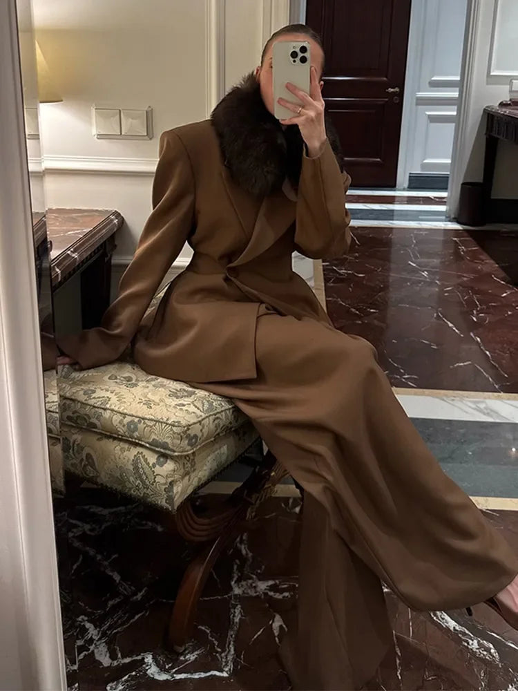 Person wearing a brown suit sitting on a chair in a room with marble floor and wooden door. Woman in a brown oversized business suit for women suit 
