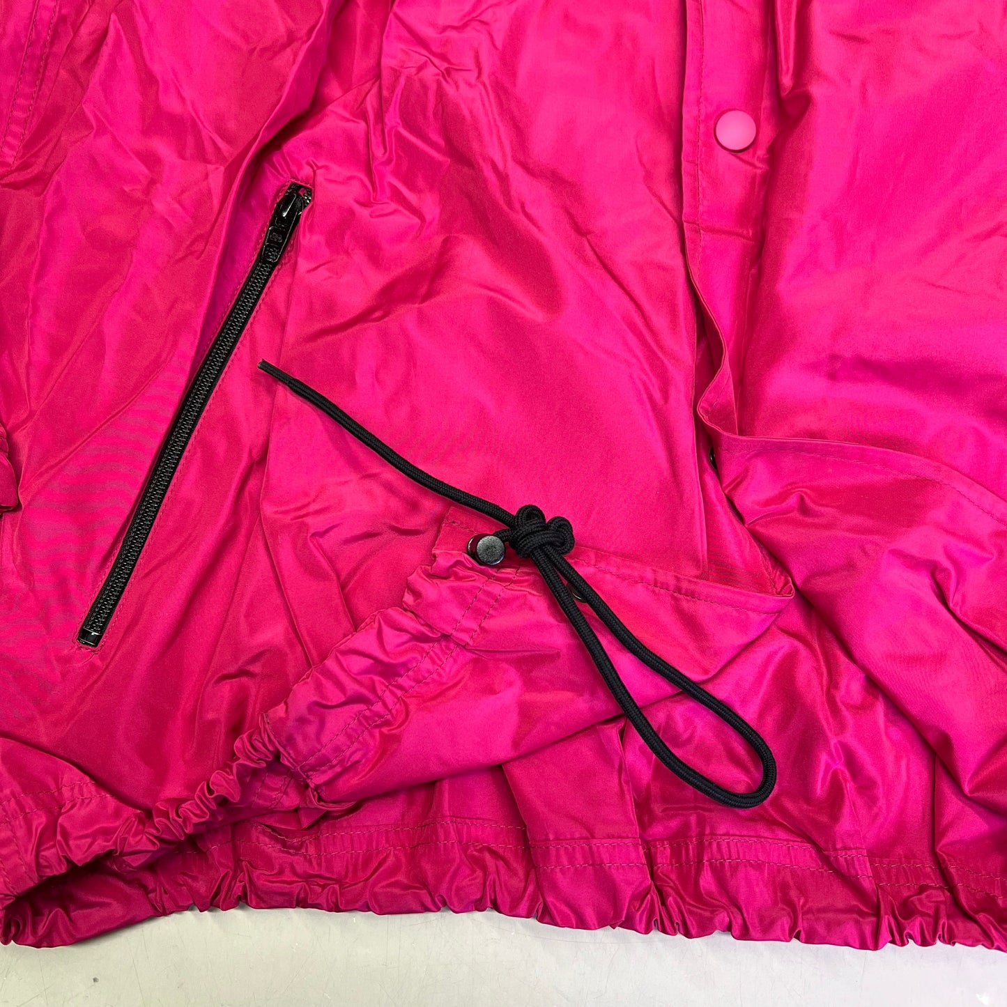 Close-up of a bright pink jacket with a black zipper and drawstring on a white background