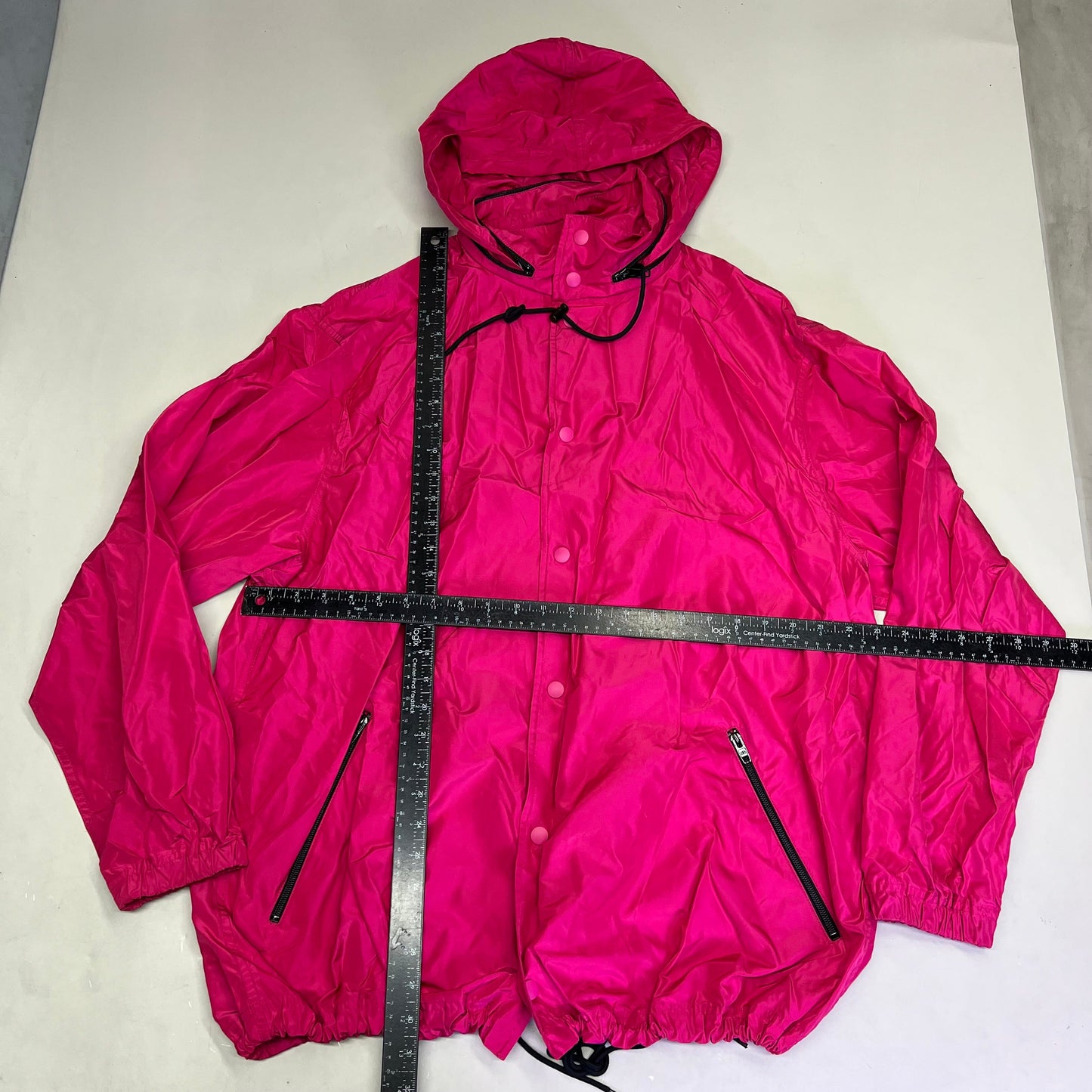 Pink raincoat with a measuring tape laid across it on a light gray background