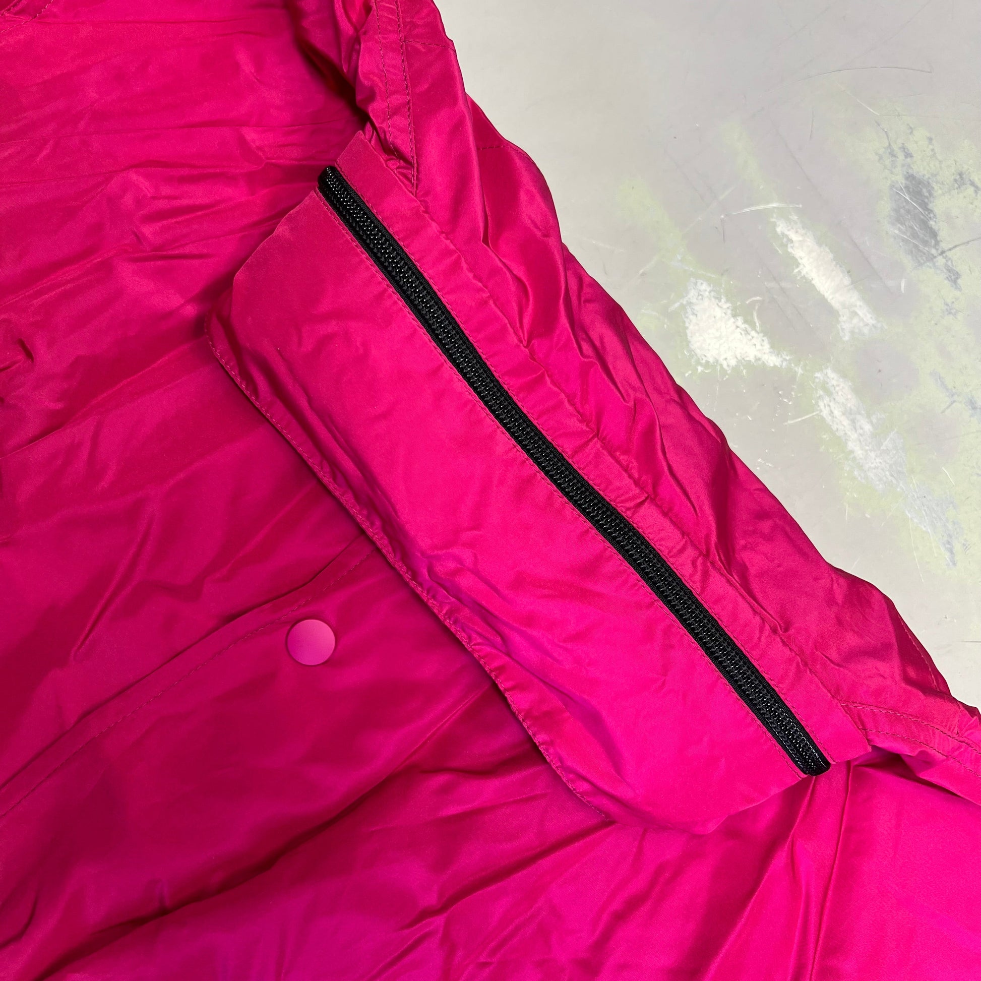 Close-up of a bright pink jacket with a black zipper on a light gray background