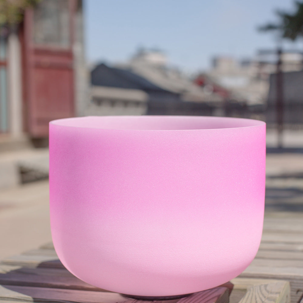 Pink crystal sound bowl on a reflective surface with a blurred outdoor background