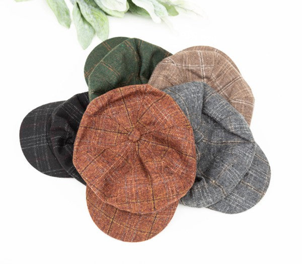 Top view of four plaid newsboy caps in black, gray, rust, and tan with classic vintage styling and short curved brims displayed on a white background.
