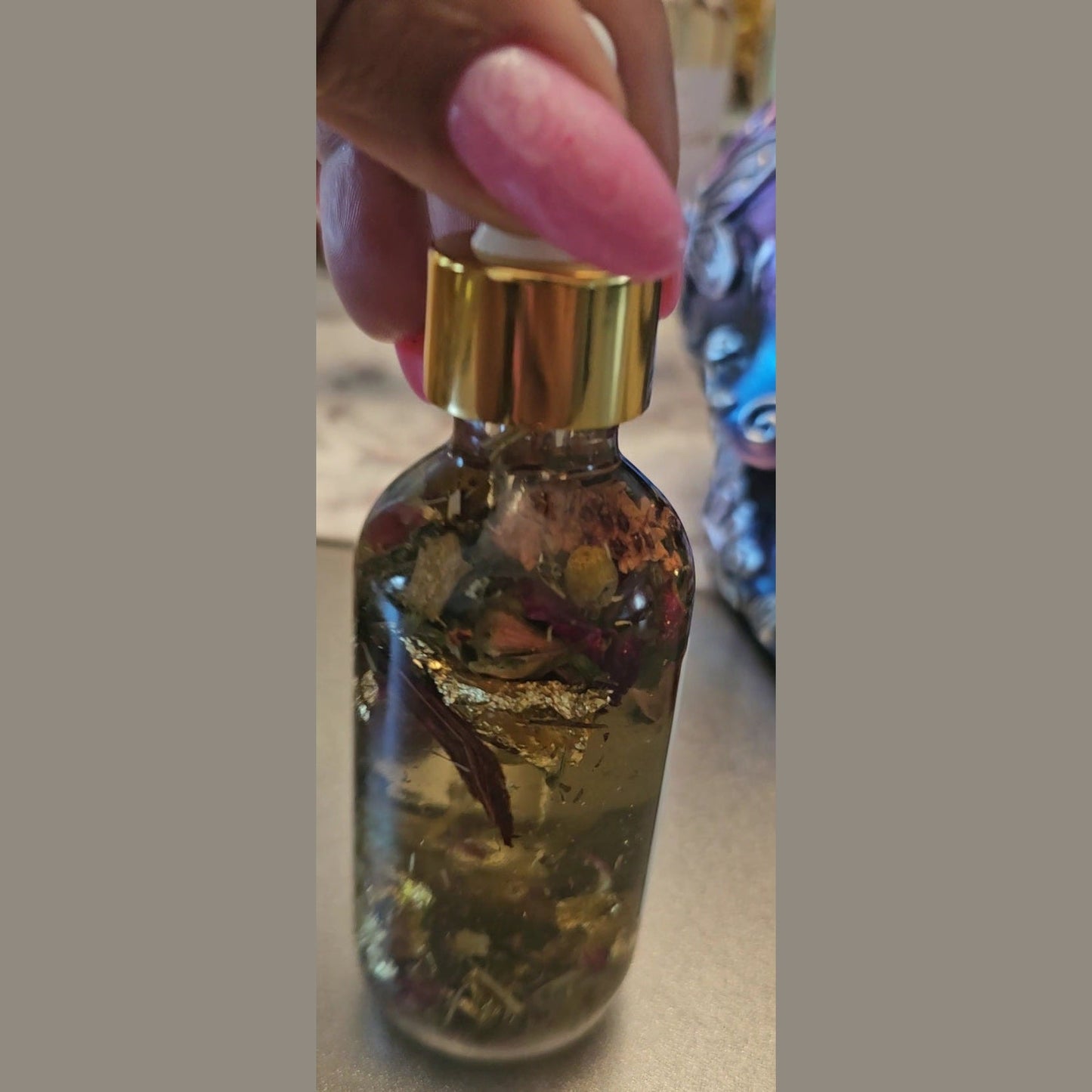 Bottle with gold cap containing herbs or spices, held by a hand. Raven Hoodoo Conjure Oil for Intuition, Manifestation, & Spiritual Power Ritual Oil