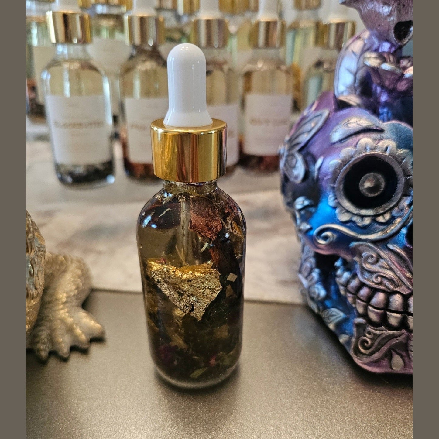 Glass dropper bottle with gold cap on a surface with decorative items in the background. Raven Hoodoo Conjure Oil for Intuition, Manifestation, & Spiritual Power Ritual Oil
