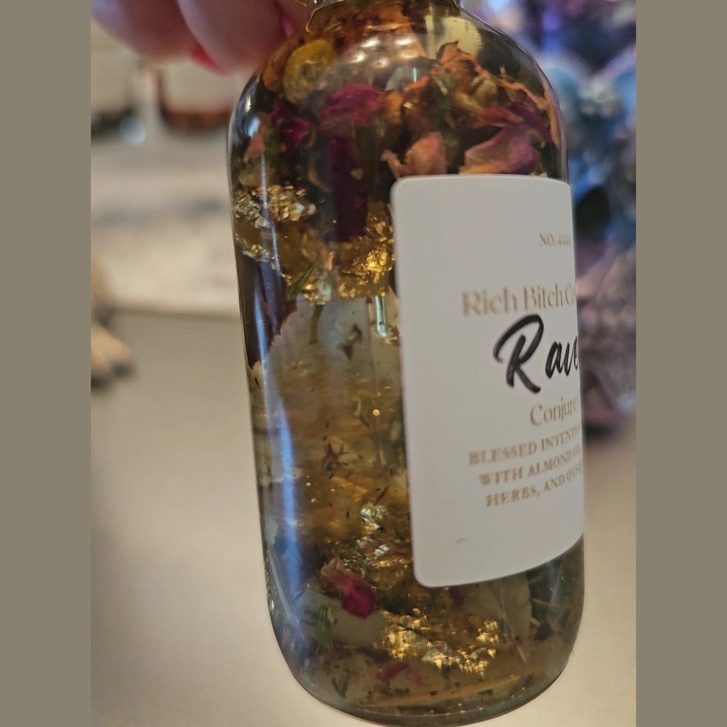 Bottle with dried flowers and herbs inside,  on a blurred background. Raven Hoodoo Conjure Oil for Intuition, Manifestation, & Spiritual Power Ritual Oil