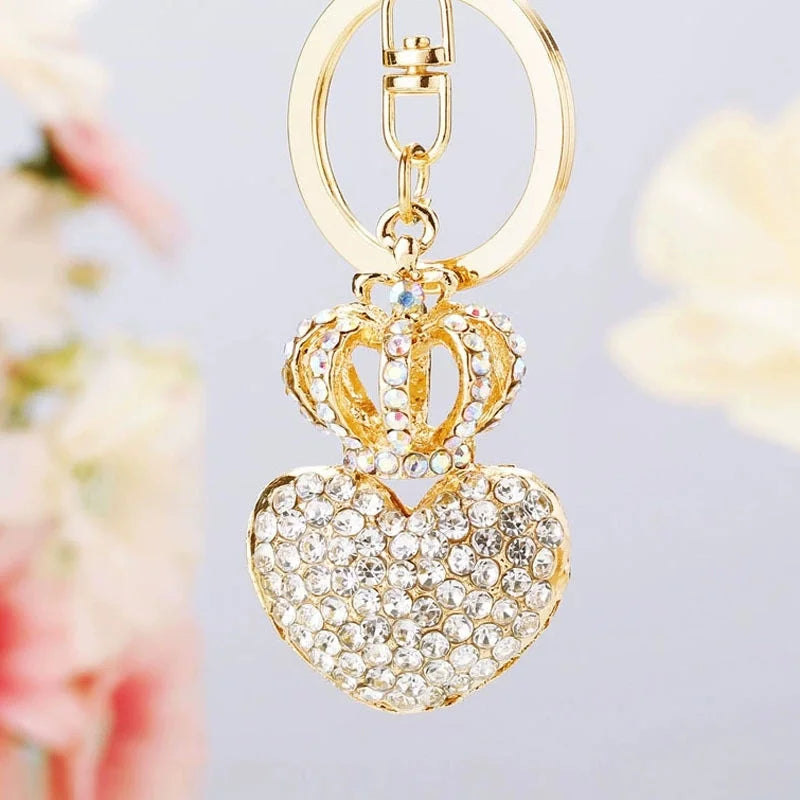 Gold-tone rhinestone heart keychain with an open crown charm attached to a polished oval key ring on a light gray background. Elegant sparkling keychain accessory for handbags, purses, backpacks, keys, and car keys.