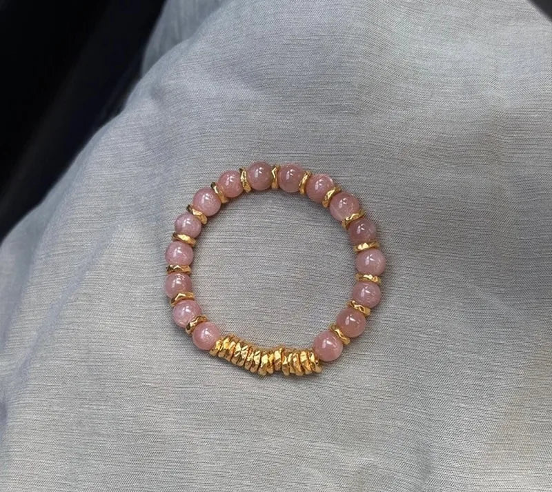 Pink beaded bracelet with gold accents on a gray fabric background