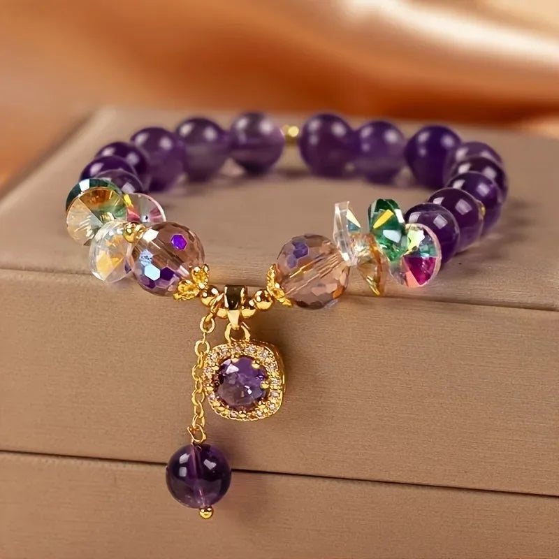 Purple beaded bracelet with gold accents and charms on a wooden surface