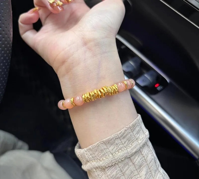 Gold bracelet with pink beads on a wrist, sitting inside a vehicle.