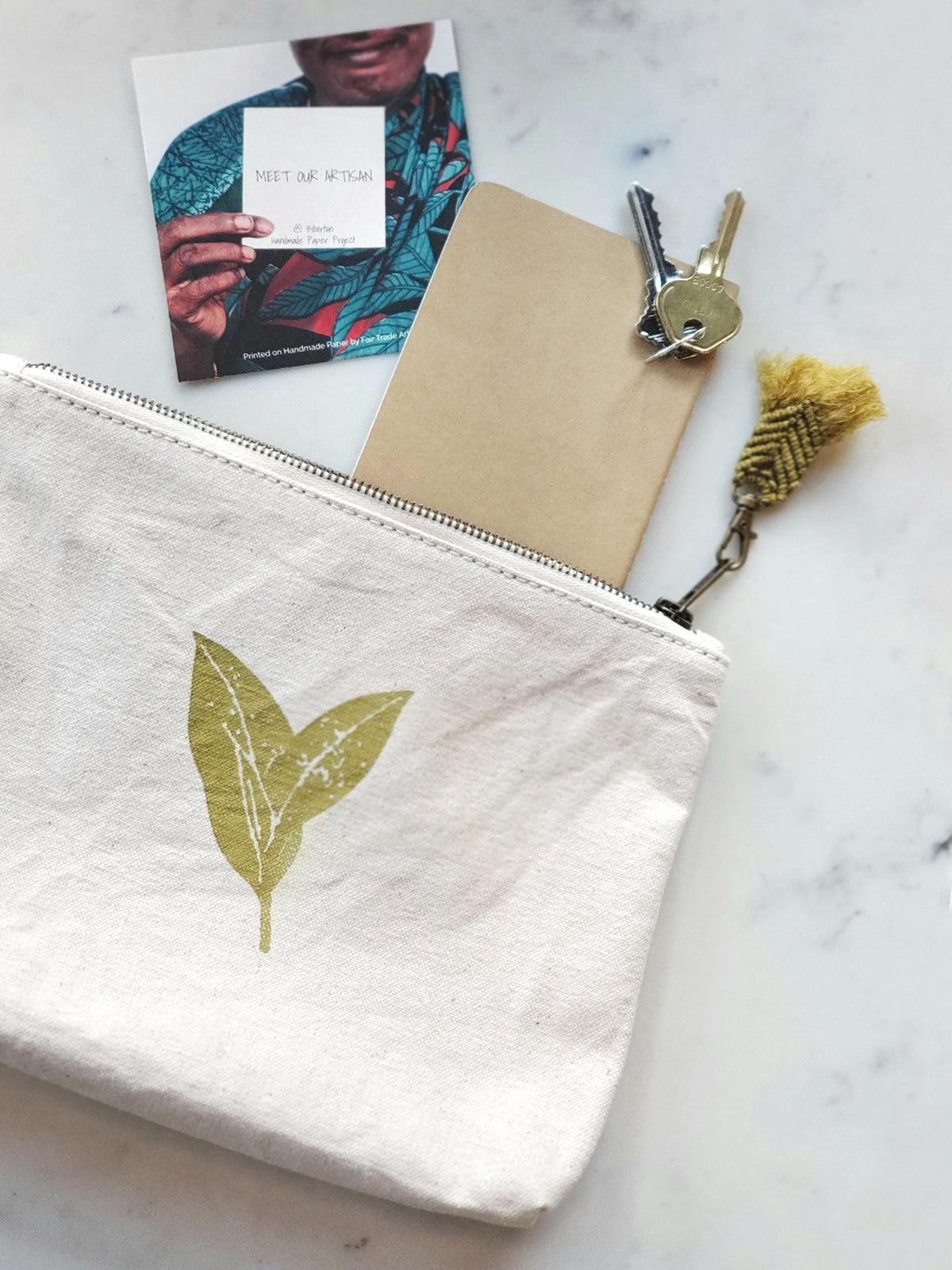 White pouch with leaf design, notebook, keys, and book on marble surface. Nature Cotton Canvas Pouch: Eco-Friendly, Ethically Sourced, Fair Trade, Handmade by Women