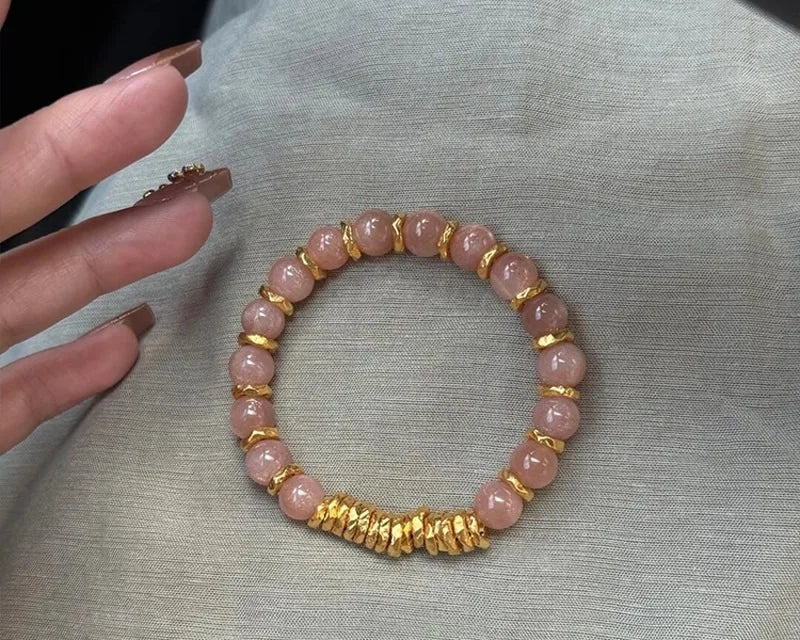 Pink beaded bracelet with gold accents on a gray fabric background