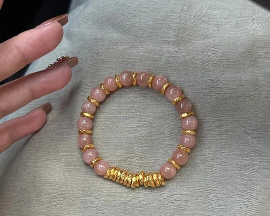 Pink beaded bracelet with gold accents on a gray fabric background
