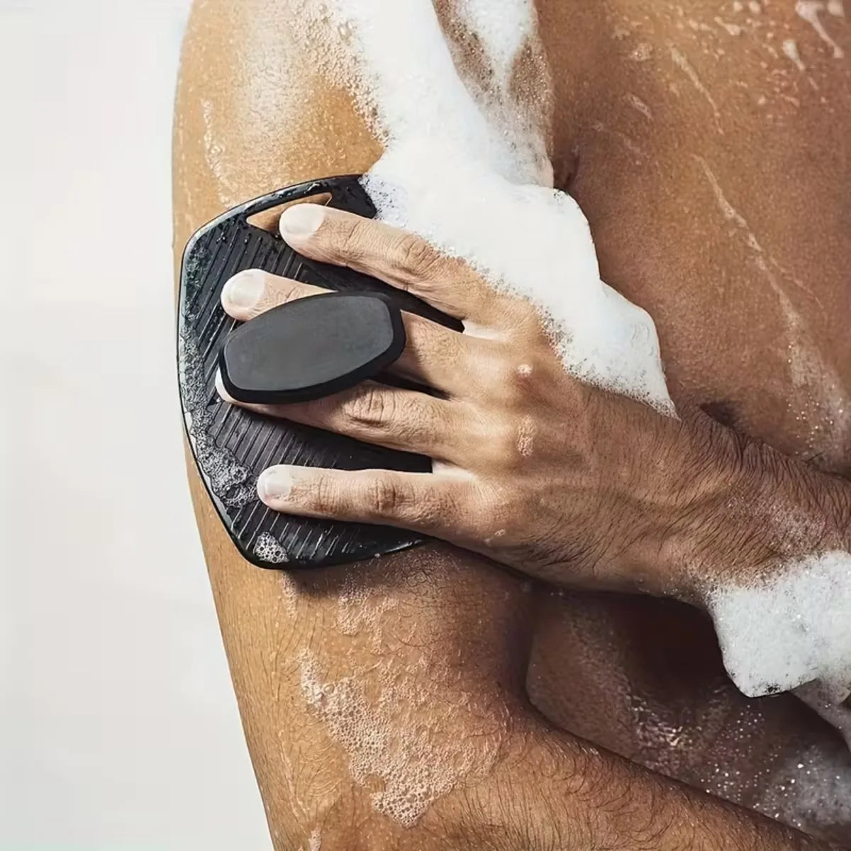 Person using a black exfoliating tool on their leg with soap suds.