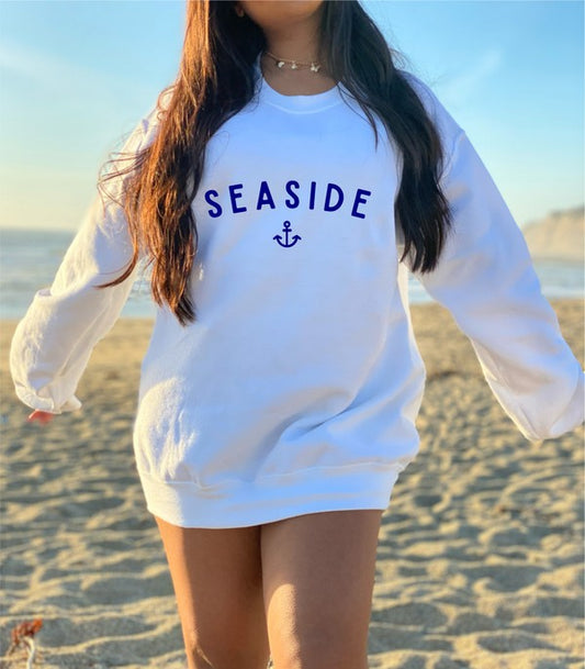 Person wearing a white sweatshirt with 'Seaside' text on a beach