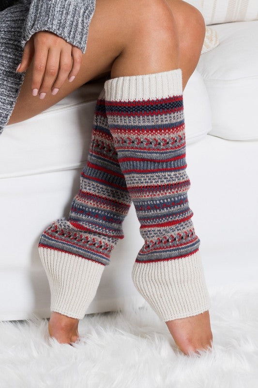 Woman wearing multicolor Fair Isle knit leg warmers featuring a classic Nordic-inspired pattern in red, gray, navy, and cream tones. These soft acrylic leg warmers showcase a thick ribbed cuff and cozy textured knit construction, providing warmth and comfort for cold-weather styling. Perfect for pairing with boots, leggings, jeans, tights, and winter outfits, these fashionable leg warmers add a rustic cabin-chic touch to everyday wear. Ideal for fall and winter fashion, holiday outfits, ski lodge getaways, 