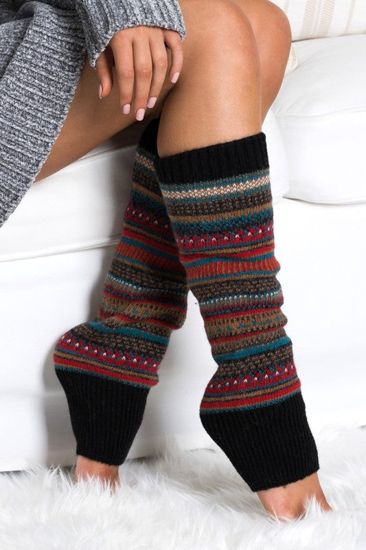 Woman wearing multicolor Fair Isle knit leg warmers featuring a classic Nordic-inspired pattern in red, gray, navy, and cream tones. These soft acrylic leg warmers showcase a thick ribbed cuff and cozy textured knit construction, providing warmth and comfort for cold-weather styling. Perfect for pairing with boots, leggings, jeans, tights, and winter outfits, these fashionable leg warmers add a rustic cabin-chic touch to everyday wear. Ideal for fall and winter fashion, holiday outfits, ski lodge getaways, 