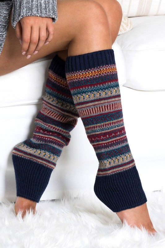 Woman wearing multicolor Fair Isle knit leg warmers featuring a classic Nordic-inspired pattern in red, gray, navy, and cream tones. These soft acrylic leg warmers showcase a thick ribbed cuff and cozy textured knit construction, providing warmth and comfort for cold-weather styling. Perfect for pairing with boots, leggings, jeans, tights, and winter outfits, these fashionable leg warmers add a rustic cabin-chic touch to everyday wear. Ideal for fall and winter fashion, holiday outfits, ski lodge getaways, 