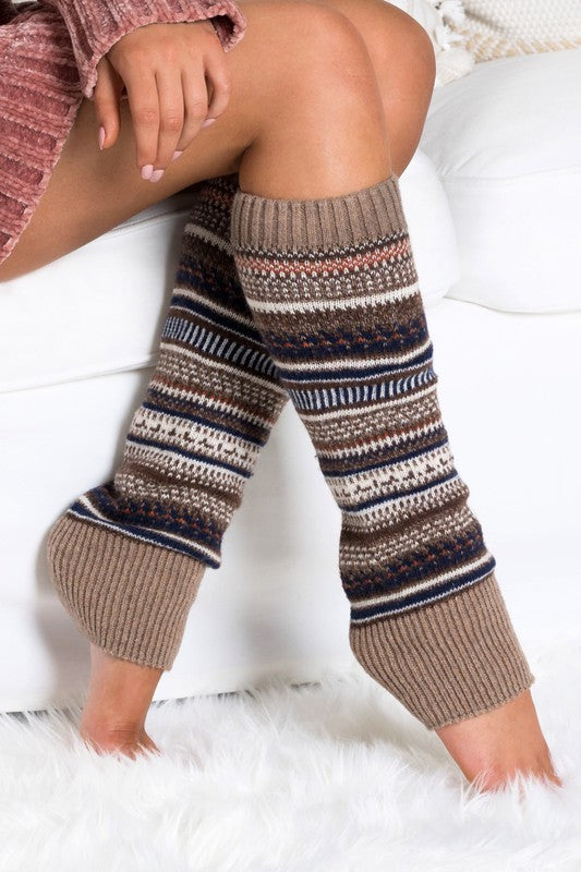 Woman wearing multicolor Fair Isle knit leg warmers featuring a classic Nordic-inspired pattern in red, gray, navy, and cream tones. These soft acrylic leg warmers showcase a thick ribbed cuff and cozy textured knit construction, providing warmth and comfort for cold-weather styling. Perfect for pairing with boots, leggings, jeans, tights, and winter outfits, these fashionable leg warmers add a rustic cabin-chic touch to everyday wear. Ideal for fall and winter fashion, holiday outfits, ski lodge getaways, 