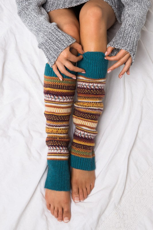 Woman wearing multicolor Fair Isle knit leg warmers featuring a classic Nordic-inspired pattern in red, gray, navy, and cream tones. These soft acrylic leg warmers showcase a thick ribbed cuff and cozy textured knit construction, providing warmth and comfort for cold-weather styling. Perfect for pairing with boots, leggings, jeans, tights, and winter outfits, these fashionable leg warmers add a rustic cabin-chic touch to everyday wear. Ideal for fall and winter fashion, holiday outfits, ski lodge getaways, 