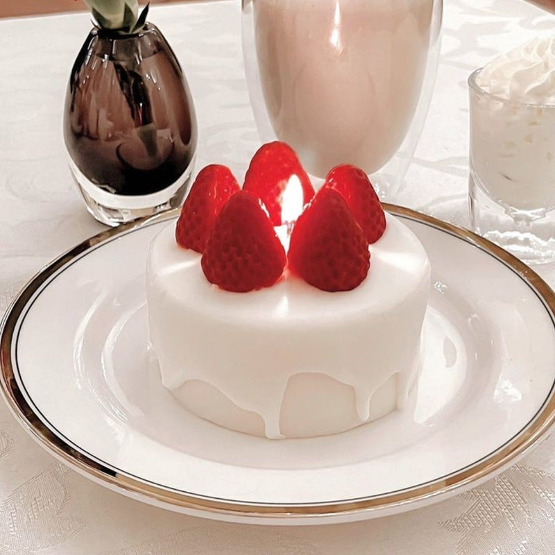Small white cake with red strawberries on a white plate with gold rim, placed on a tablecloth. Handmade Strawberry Cake Shaped Candle Soy Wax Aromatherapy
