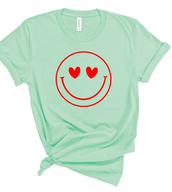 Mint green Bella+Canvas unisex T-shirt featuring a bold red smiley face graphic with heart-shaped eyes, styled with rolled sleeves and a knotted front on a clean white background for a fun, playful casual look.