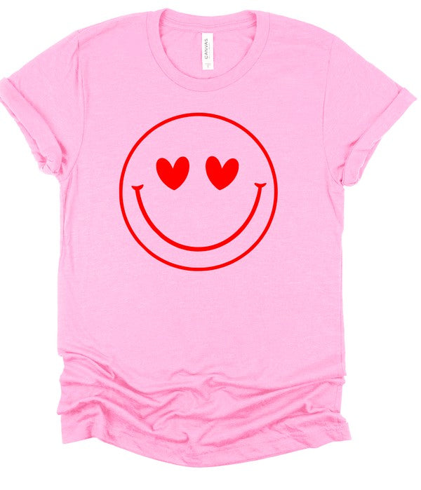Light pink Bella+Canvas unisex T-shirt featuring a bold red smiley face graphic with heart-shaped eyes, displayed with rolled sleeves and a knotted hem on a clean white background for a fun, playful, casual style.