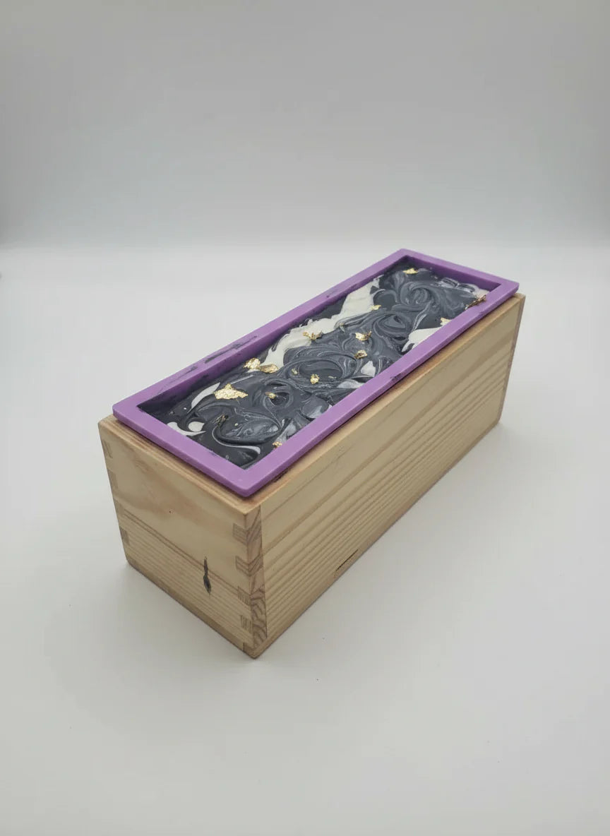 Sophisticated tuxedo-inspired handmade soap bar in a wooden mold with black and white swirled design and purple silicone liner, displayed on a white background.