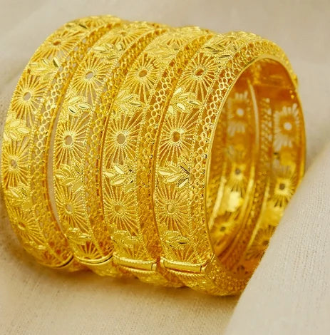 Three gold bangles with intricate designs on a beige background