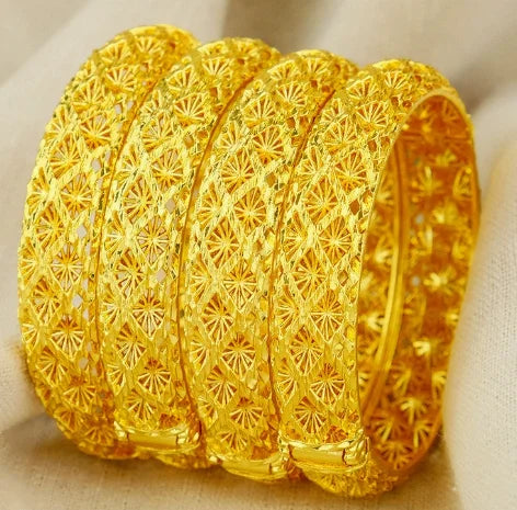 Three gold bangles with intricate designs on a beige background