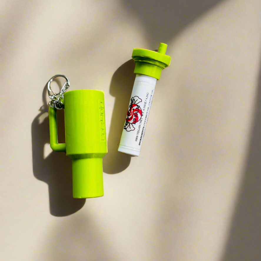 Green silicone tumbler-style lip balm holder keychain with detachable lip balm tube, designed to clip onto keys, purses, backpacks, and handbags for easy everyday access.