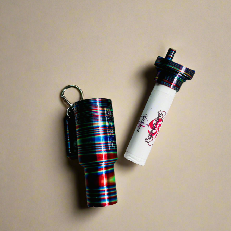 Colorful striped silicone tumbler-style lip balm holder keychain displayed beside a white lip balm tube on a beige background.