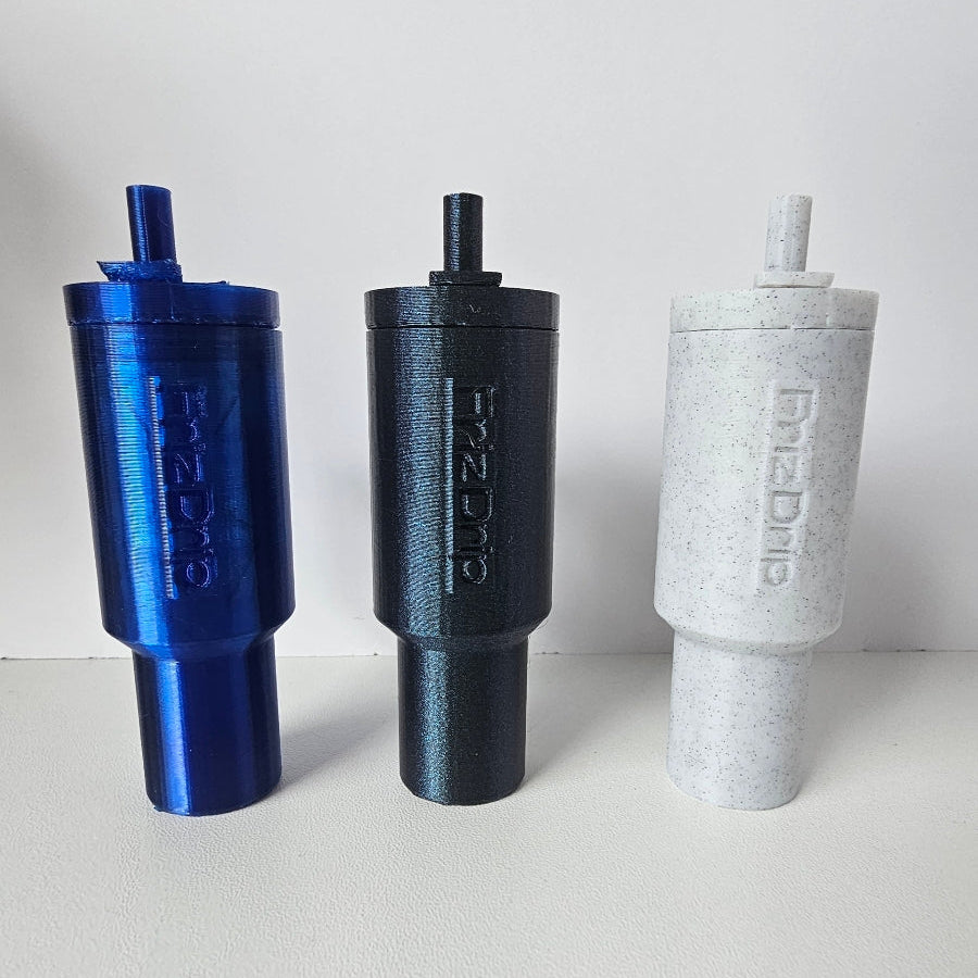 Blue, black, and white tumbler-style silicone lip balm holder keychains displayed upright on a white surface, designed to attach to keys, purses, backpacks, and bags for easy access to standard lip balm tubes.