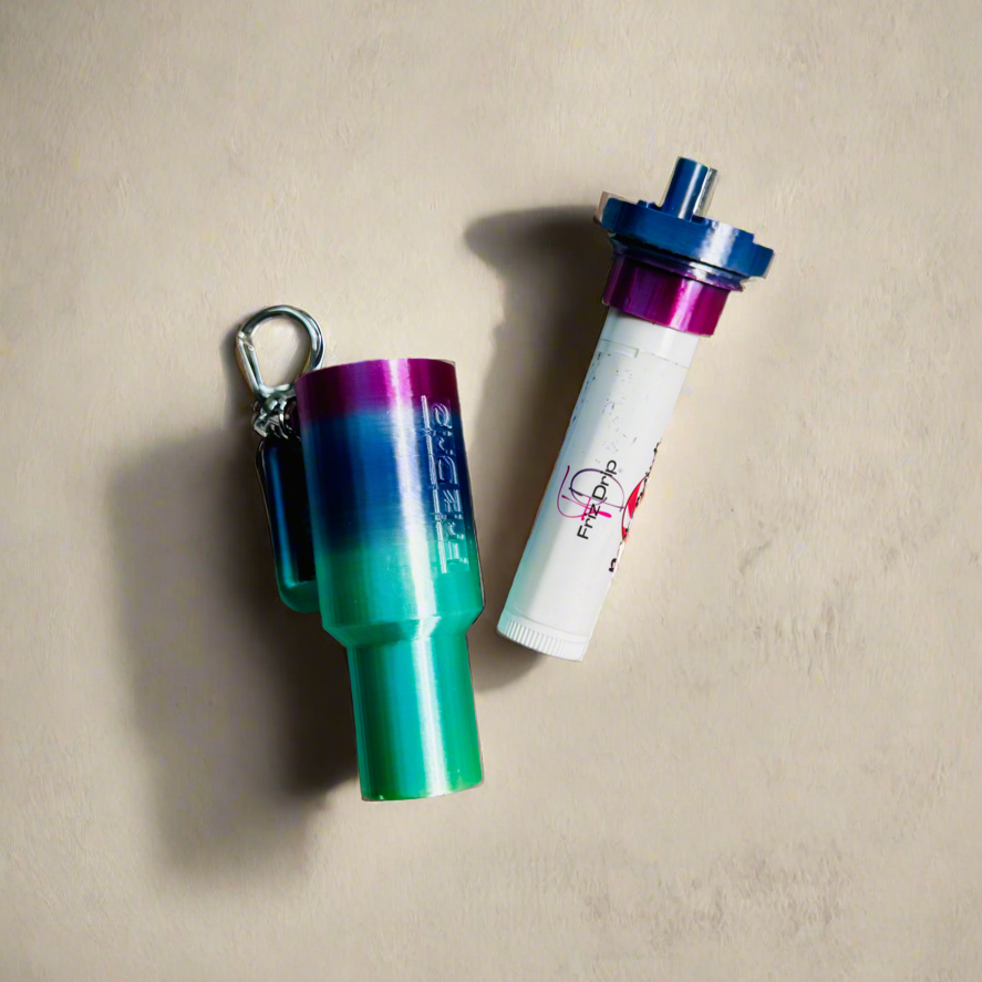 Gradient tumbler-style silicone lip balm holder keychain displayed beside a standard lip balm tube on a light background, featuring a secure key ring for attaching to purses, backpacks, totes, or keys.