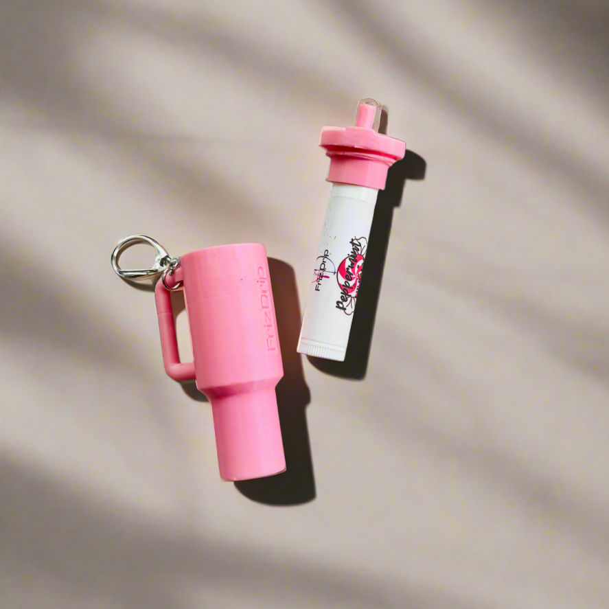 Pink silicone tumbler-style lip balm holder keychain with matching lip balm, featuring a durable key ring for attaching to purses, backpacks, totes, or keys on a neutral background.